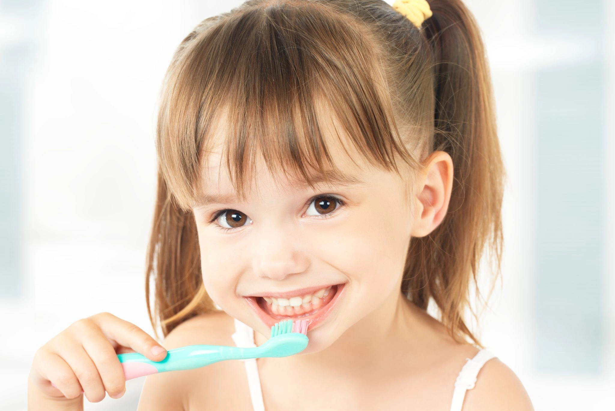 Young girl smiling smiling while brushing her teeth