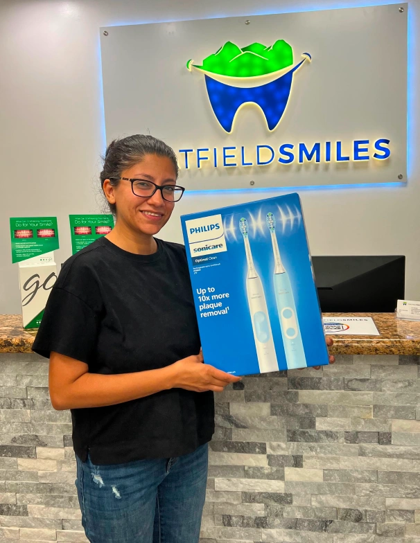 Patient holding a Philips Sonicare electric toothbrush gift box while smiling at the reception desk of Chatfield Smiles dental office.