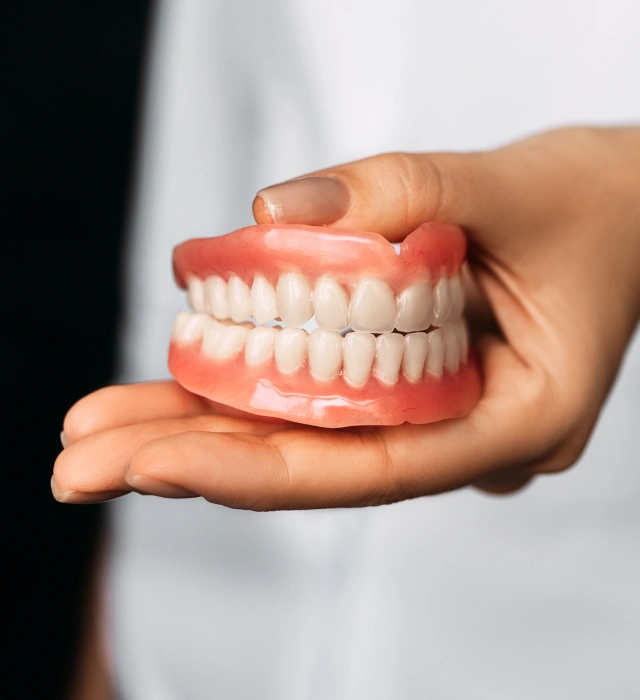 A hand holding a full set of custom dentures at Chatfield Smiles Dentistry in Littleton, CO